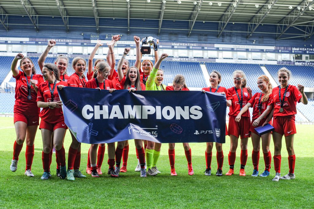 A winning girls' team lifting the trophy and holding the winners' banner after becoming National Champions at West Bromwich Albion FC