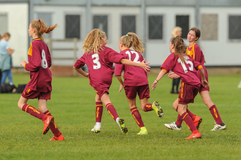 5 team mates running across a football pitch together in the U13 girls' cup competition