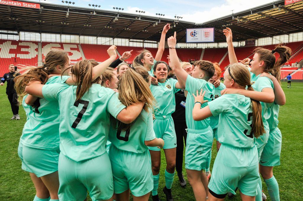 Park View's U18 Women's Super League team in their mint green kit, celebrating becoming National Champions on the pitch at Stoke City FC