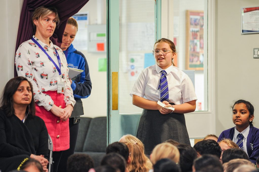 A school pupil standing up in assembly, reading out her question to Faye White